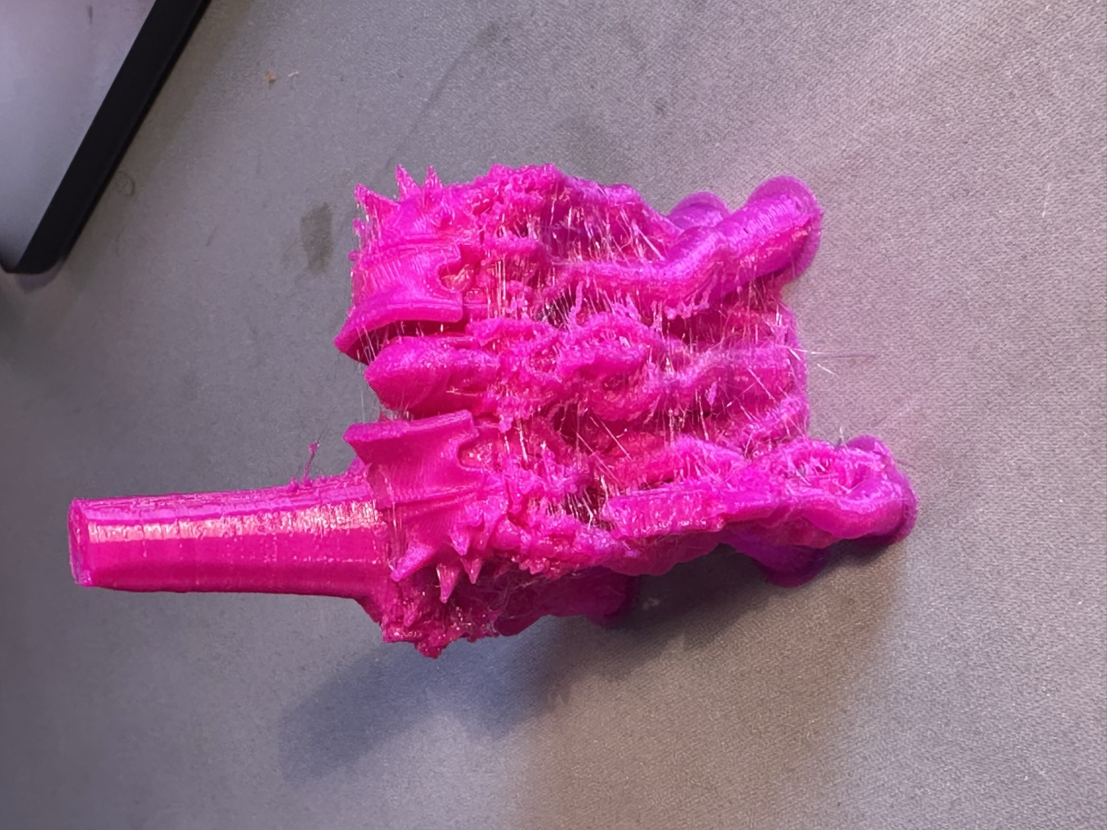 A small magenta 3D-printed orc figure with a tall support pillar behind it and a web of fine printed threads across its body